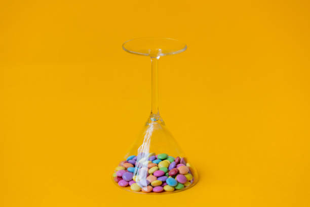 A lot of candy canes are scattered from an overturned glass goblet. Multi-colored candies in a glass on a black background.
