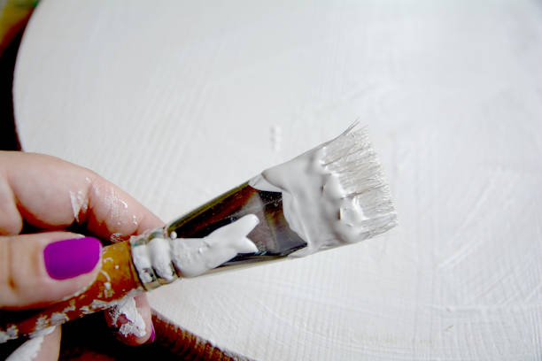 istock Priming of a wooden panel for painting with white acrylic primer using a bristle brush. Hands in the frame. 1164950764