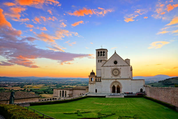 basilica di san francesco d'assisi al tramonto sotto splendidi cieli arancioni e blu, italia - umbria foto e immagini stock