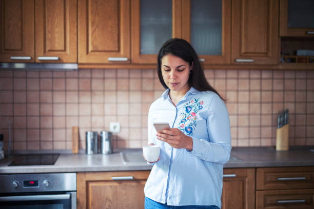 istock Beautiful woman holding coffee cup and using phone at home. 1164961841