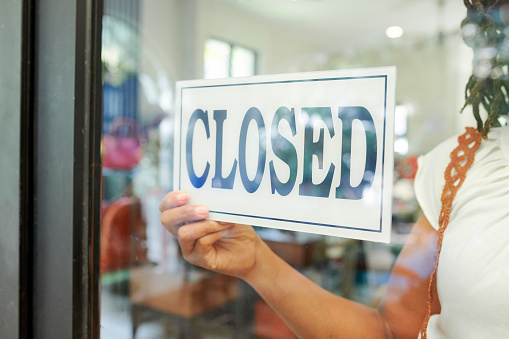 Close-up of saleswoman hanging the Closed sign on glass door and closed the store