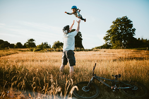 A father and his little girl take a break from a mountain bike ride, the dad tossing his girl high into the air.  A fun way to spend time together and exercise while on vacation in the Seattle, Washington area.