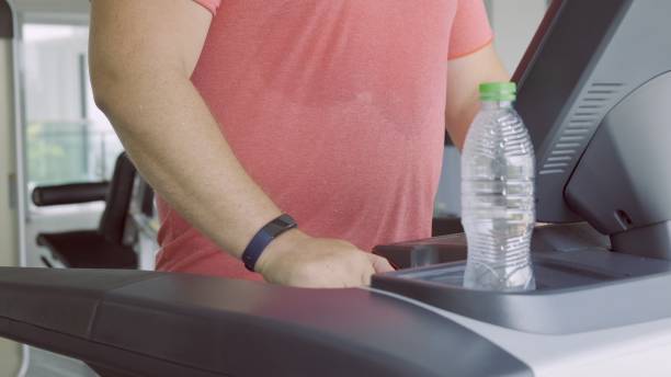 istock chubby man walking on running track, warming up on gym treadmill. 1164963952