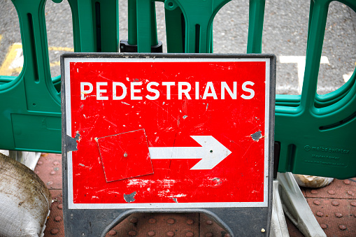 Red and white road sign with arrow on a pavement / sidewalk on London Road in Mitcham, Surrey. Pedestrians keep to the right of the warning sign.