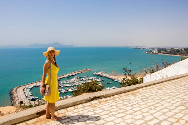 Young woman in yellow dress Young woman in yellow dress in Sidi Bou Said. On background mediterranean sea with yachts and boats in old port tunisia beach stock pictures, royalty-free photos & images