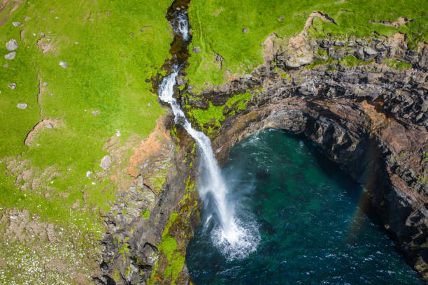 Aerial view of Mulafossur waterfall in Gasadalur village in Faroe Islands, North Atlantic Ocean. Photo made by drone from above. Nordic Natural Landscape. Aerial view of Mulafossur waterfall in Gasadalur village in Faroe Islands, North Atlantic Ocean. Photo made by drone from above. Nordic Natural Landscape. vágar photos stock pictures, royalty-free photos & images