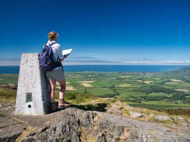 Photo of A lone walker at the top of Garn Fadryn checks a map while facing Nefyn on the Llyn Peninsula, Gwynedd, Wales, UK