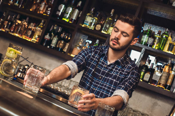 istock Young bartender standing at bar counter holding glasses thoughtful 1165006416
