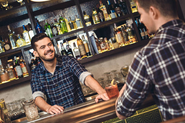 istock Young bartender standing at bar counter with customer talking cheerful 1165006427