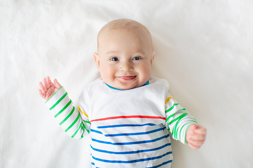 Baby boy on white blanket. Infant child after sleep. Kid in bed. Adorable newborn relaxing after nap. Bedding and clothing for kids. Children care.