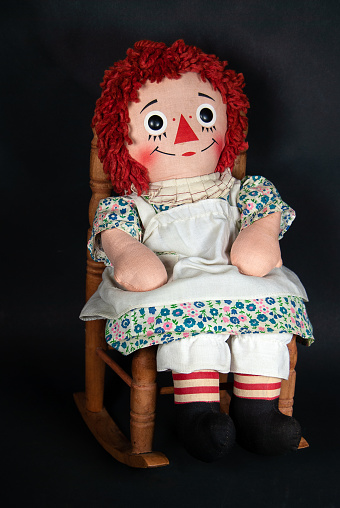 old rag doll with white apron sitting in a wooden rocking chair