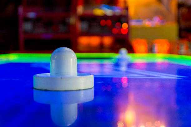 Air Hockey Game at an Arcade This closeup picture shows the paddle for an air hockey game in an arcade.  Out of focus are the colorful games in the arcade that surround the air hockey table. arcade photos stock pictures, royalty-free photos & images