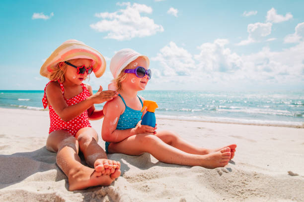 sun protection, cute girls with sun cream at beach stock photo