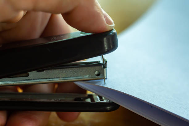 istock Woman's left hand holding stapler and stapling white paper on wooden background, Problem Process, Close up & Macro shot, Selective focus, Office Stationery concept 1165020765