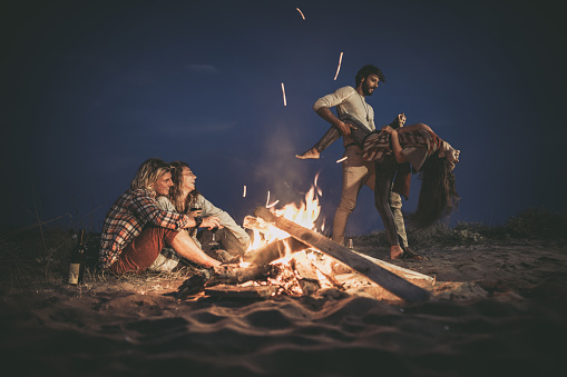 Young happy couples having fun on a beach party by the campfire at night. Copy space.