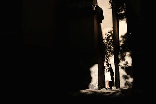 stylish woman standing in sunlight and shadows at old building  in european city street, space for text