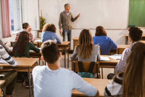 istock Back view of large group of high school students on a class in the classroom. 1165039399