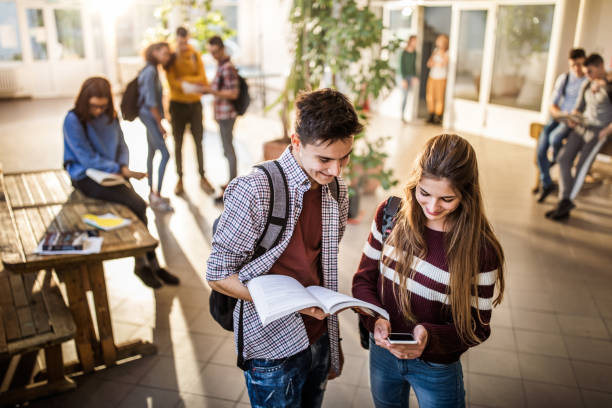 istock Happy high school couple using cell phone in a hallway. 1165040057