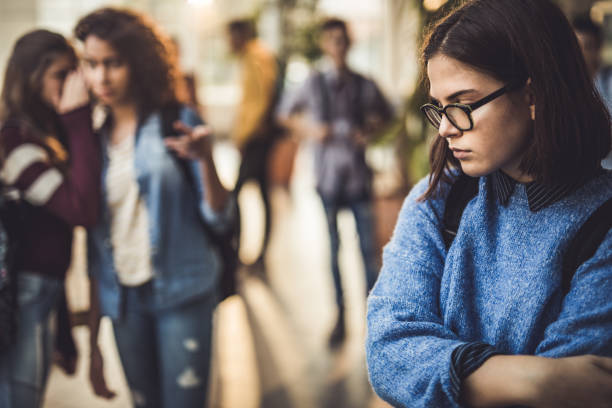 Sad high school student feeling lonely in a hallway. Displeased female student bullied by her classmate standing alone in a hallway. stereotypical stock pictures, royalty-free photos & images