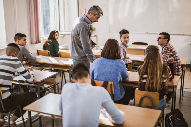 istock Mid adult teacher assisting his students on a class at high school. 1165040469