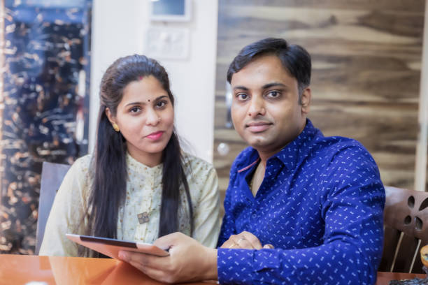портрет молодой пары, сидящей с цифровым планшетом дома - digital tablet indian ethnicity young couple computer стоковые фото и изображения