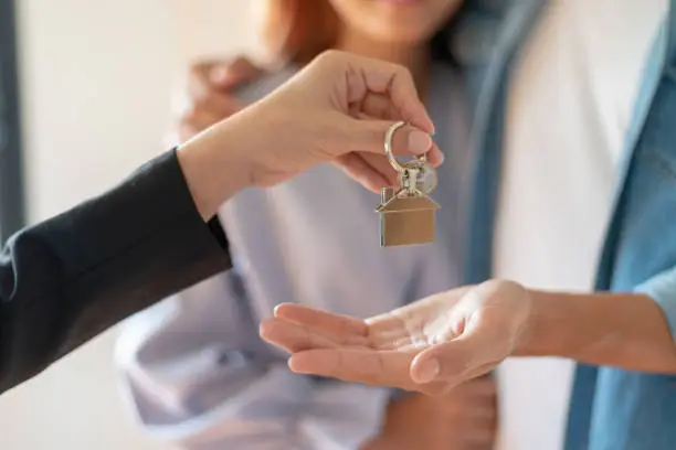 Photo of Young Asian couple receiving new apartment or room key from Real Estate Agent or real estate sales agent after finish a rental or buying contract.