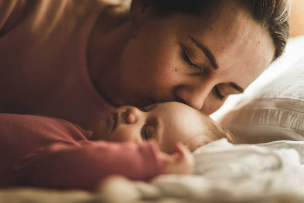 istock Affectionate mother kissing her newborn baby girl while she is sleeping 1165042221