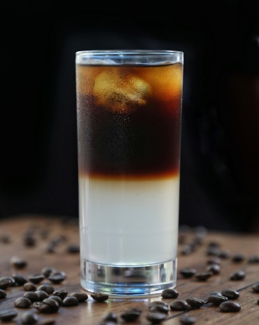 Coffee tonic in a tall glass with coffee beans lying around.