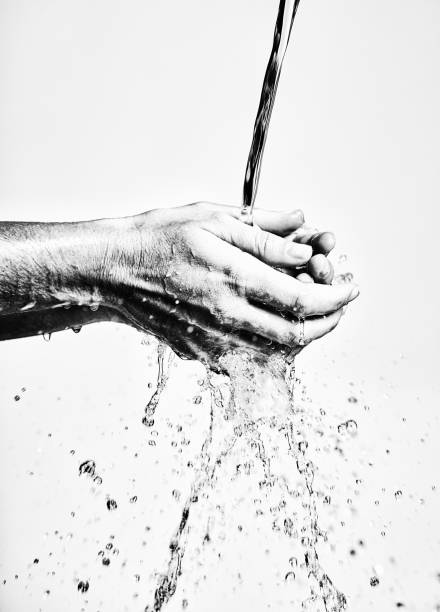 Hands being washed under running water, seen in black and white against a white background.