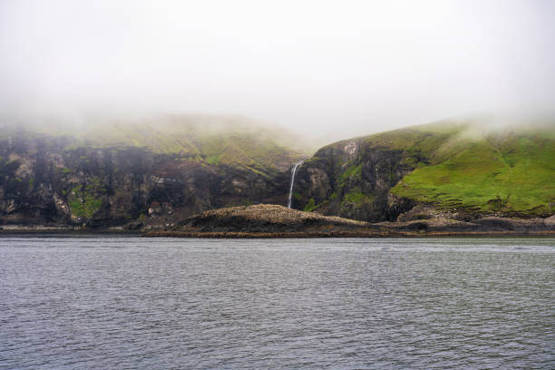 A waterfall flowing into Atlantic Ocean and thick fog covers green cliffs. Vagar, Faroe Islands. Vagar, Faroe Islands. mykines faroe islands photos stock pictures, royalty-free photos & images