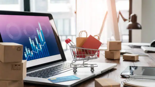 Photo of Shopping bags in shopping cart and credit card on laptop with paper boxes on table and sales data economic growth graph on screen, buying and selling services online on network, online shopping and e-commerce concept