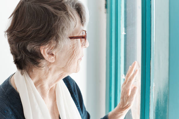istock Lonely looking senior woman looks through window 1165070259
