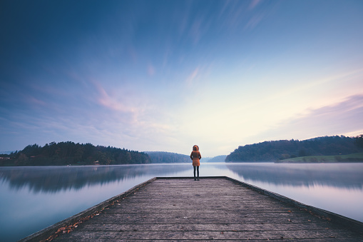 Woman standing on the jetty and watching colorful sunrise.