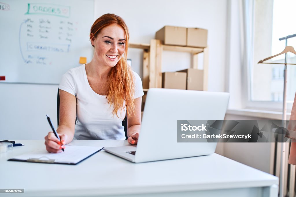 Female online business owner using laptop and documents in small office Women Stock Photo