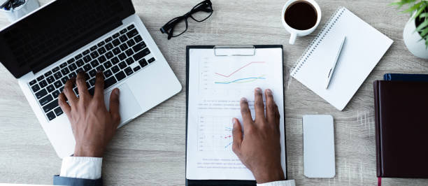 istock Unrecognizable afro businessman working on his laptop with financial reports around 1165075258