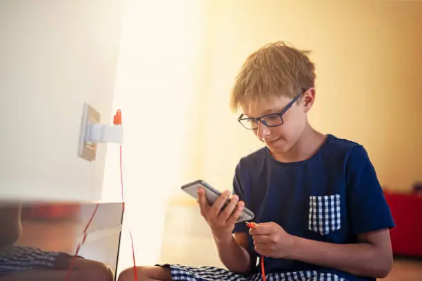 Photo of Little boy plugging smartphone to a charger at home