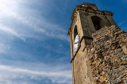 Old bell tower with clock on blue sky with clouds. Church of St. Francis, Vernazza village. Cinque Terre, Liguria, La Spezia province, Italy, Europe. UNESCO world heritage site