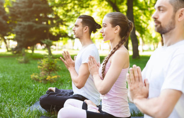 istock Three friends holding hands in namaste while practicing yoga outdoors 1165078679