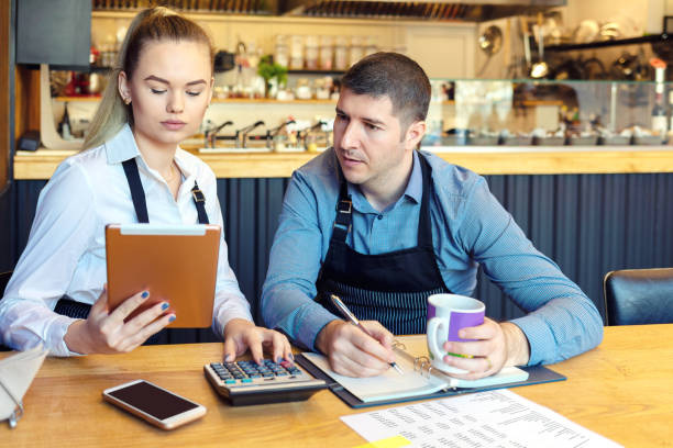 proprietários pequenos do restaurante da família que discutem finanças que calculam contas e despesas do negócio pequeno novo-homem e mulher forçados que vão através do documento junto na cafetaria - fast food restaurant restaurant cafe indoors - fotografias e filmes do acervo