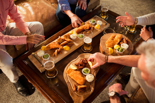 Bonding Over Fish and Chips Group of mixed age range male friends eating fish and chips and drinking casually together. pub food stock pictures, royalty-free photos & images