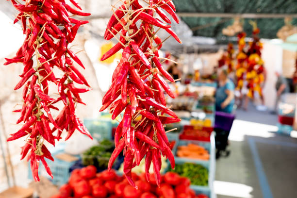 close up of red hor chili pepper hangin at organic farmers market stalls with people in background during sunny summer day stock photo