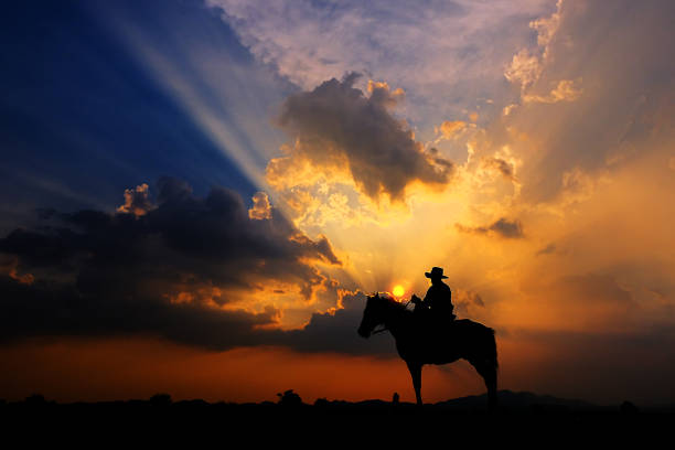 The silhouette of a cowboy on horseback at sunset on a  background stock photo