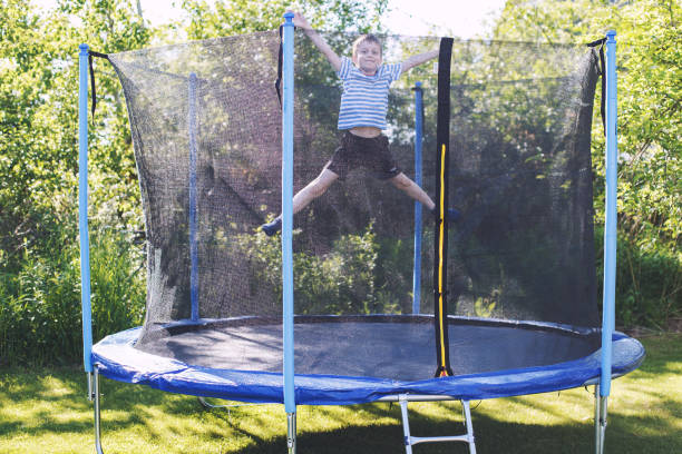 niño saltando en trampolín. el niño juega en un trampolín al aire libre - trampolín artículos deportivos fotografías e imágenes de stock