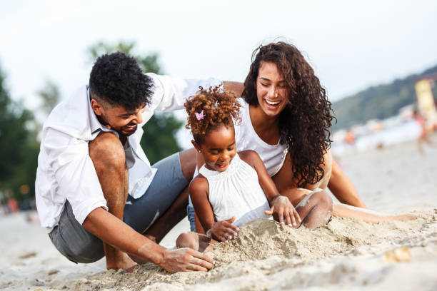 young mixed race family sitting and relaxing at the beach on beautiful summer day. - beach two parent family couple family imagens e fotografias de stock