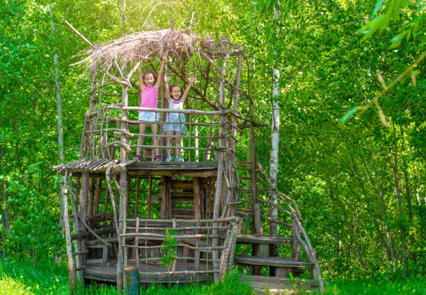Two little happy girls in a wooden tree house on a sunny day. Sisters rejoice in the summer. The concept of summer Two little happy girls in a wooden tree house on a sunny day. Sisters rejoice in the summer. The concept of summer. The sun is shining. kids play house stock pictures, royalty-free photos & images