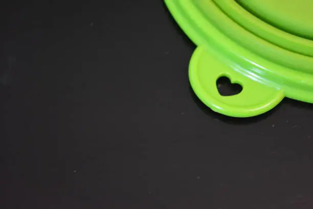 Photo of Green folding and multifunctional rubber plate, a bowl with a plastic edging on a black glossy surface.