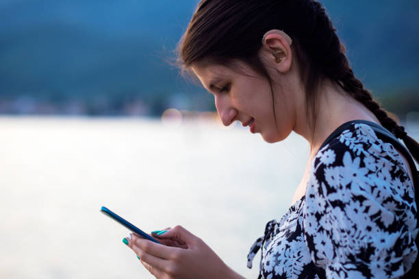 Young woman with hearing aid using mobile phone by the sea