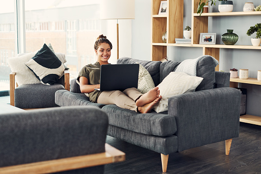 Shot of a young woman using a laptop on the sofa at home