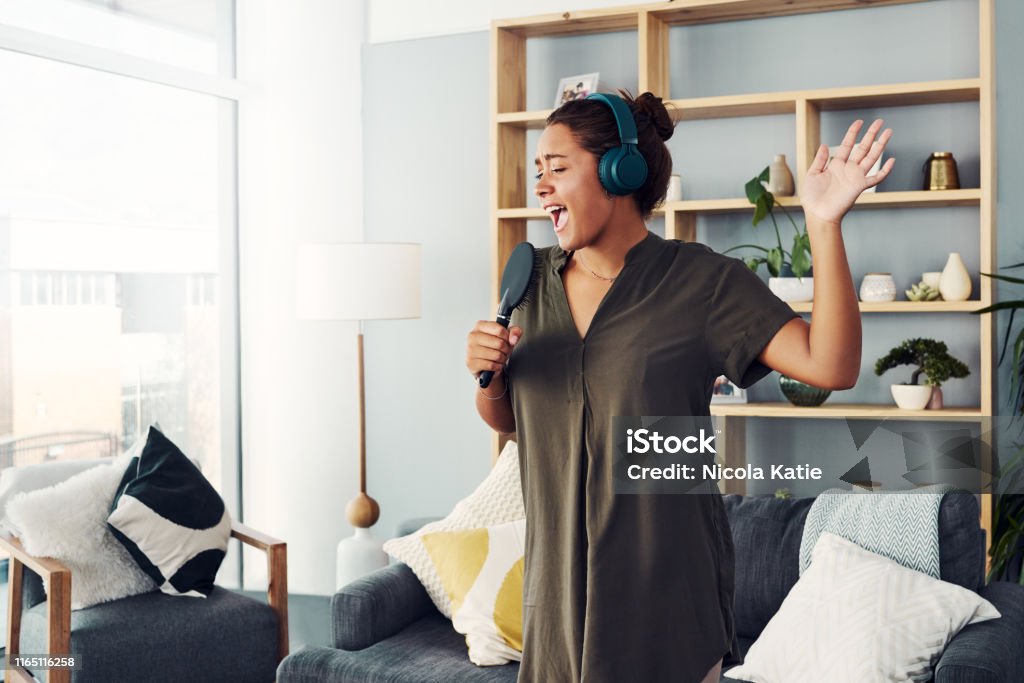 Let your inner diva shine Shot of a happy young woman singing with a microphone in the living room at home Singing Stock Photo