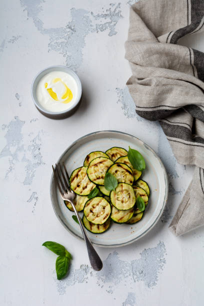istock Grilled zucchini salad with basil leaves in a simple ceramic plate on a white concrete background. Flat lay 1165119224